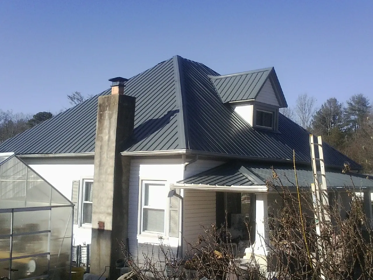 Dark blue standing seam metal roof on a white farmhouse with dormer — Slate & Tile Roof Repair by Roofing Brothers in Metter