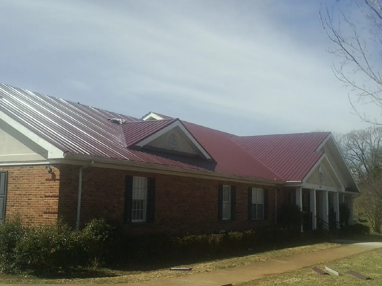 Red metal roof with gabled entries on a long brick building, from a Hail Damage Roof Repair job in Metter