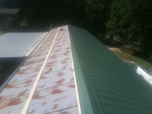 Old rusted panels beside newly installed green metal roofing — Wind Damage Roof Repair by Roofing Brothers in Metter