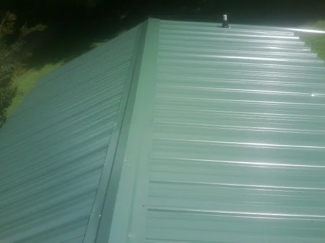 New green metal panels meeting at the ridge of a roof — Flat Roof Repair work by our crew in Metter