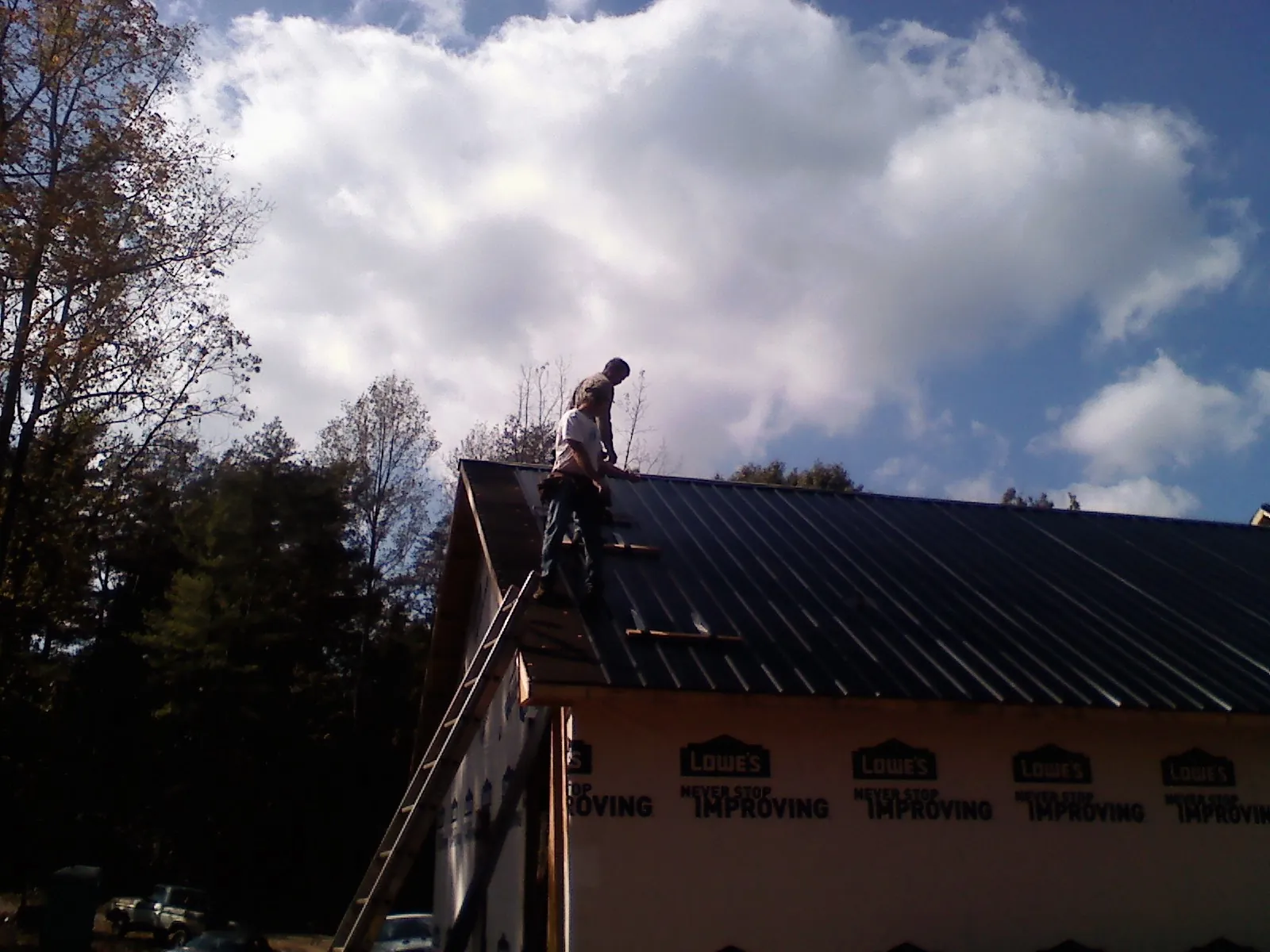 Roofer fastening dark metal panels high against a cloudy sky, from a Roof Inspection job in Metter